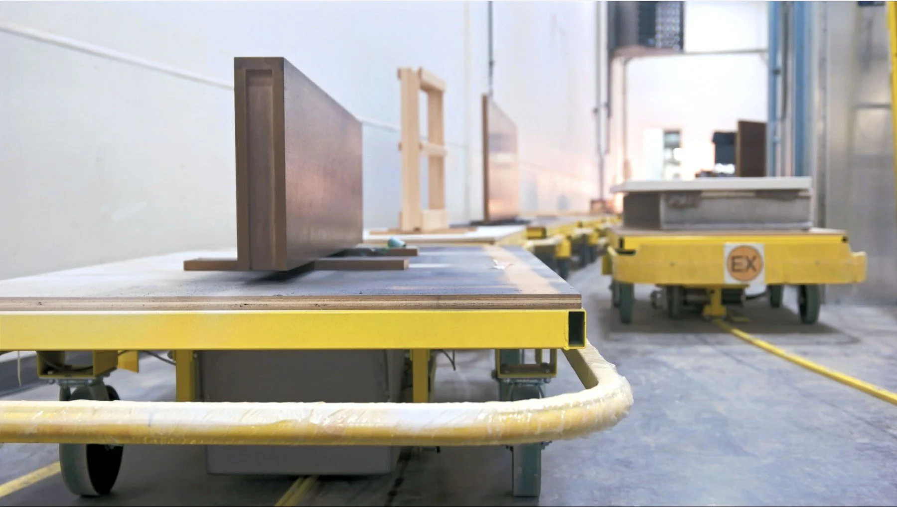 An assembly line in a manufacturing setting with yellow PowerCart Door Line carrying wooden components.