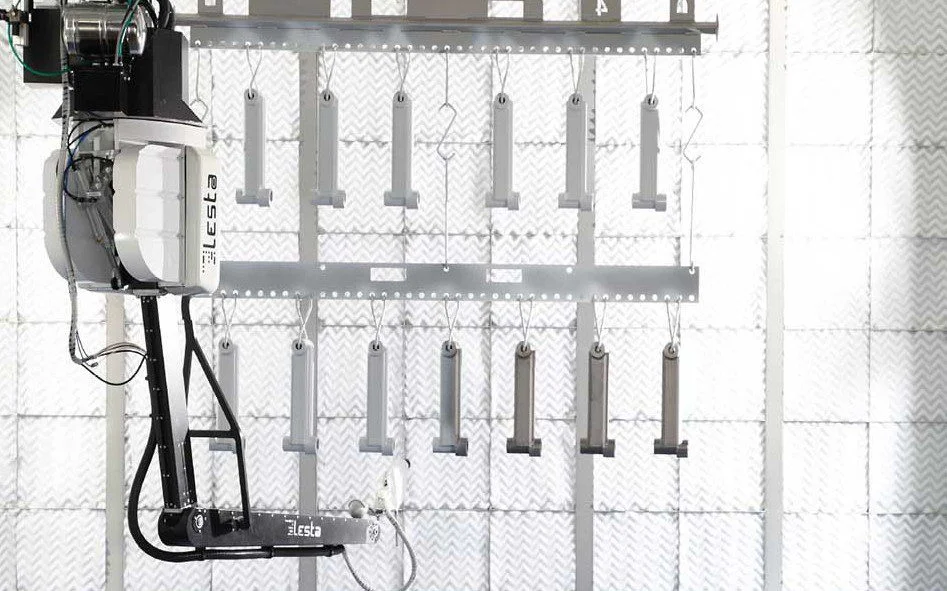 A robotic painting arm labeled "Lesta" next to hanging objects in a facility.
