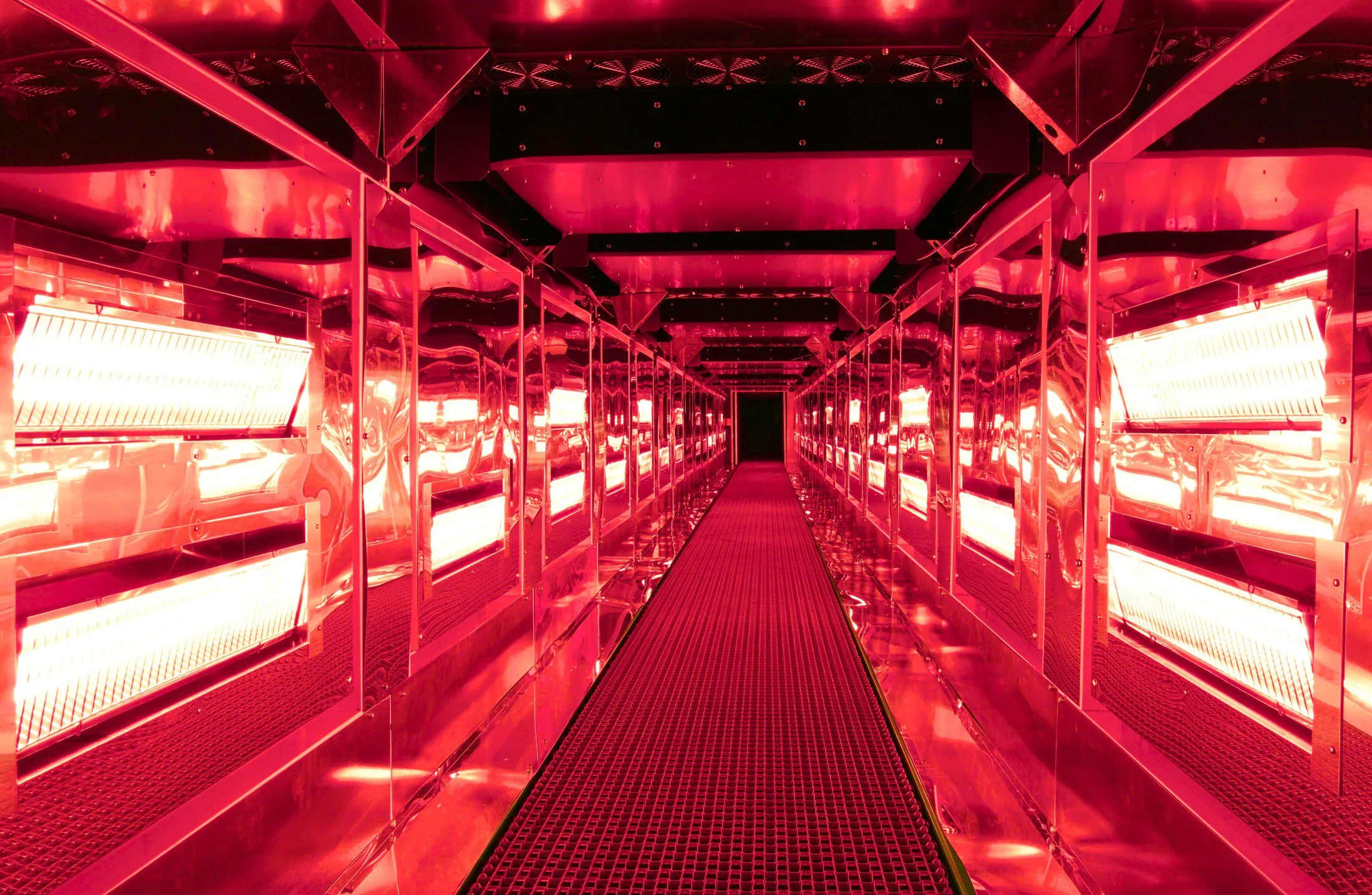 A long hallway illuminated by red lights, featuring a Halcon Tunnel Oven.